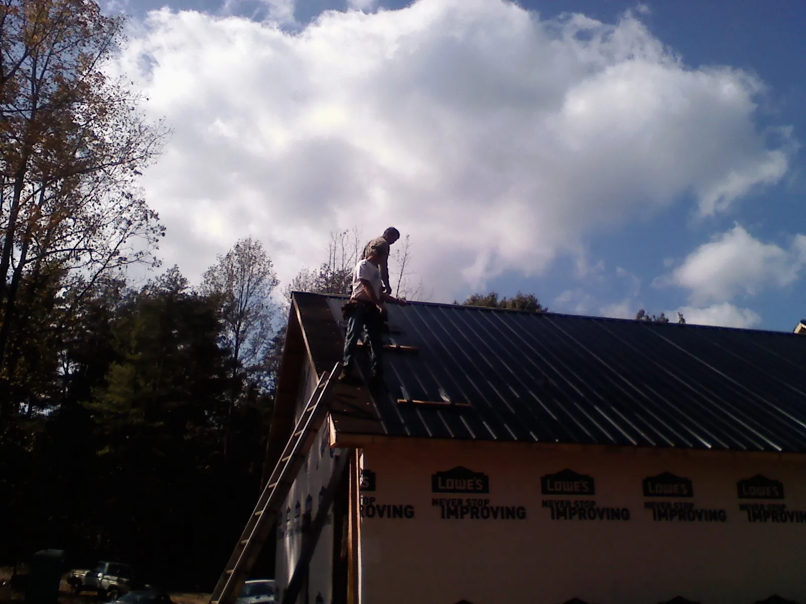 Roofer fastening dark metal panels high against a cloudy sky, from a Roof Inspection job in Rye